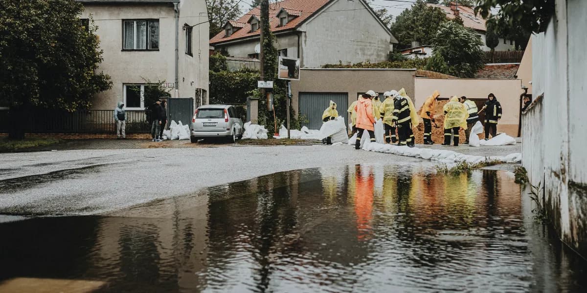 Emergency workers in high-visibility raincoats laying sandbags beside a flooded street