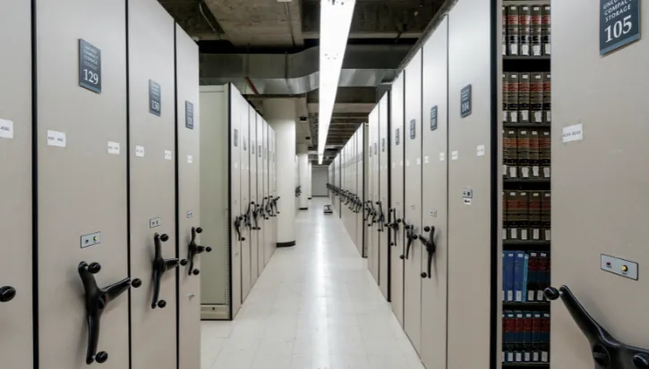 Aisle between rows of numbered grey storage cabinets under fluorescent lights