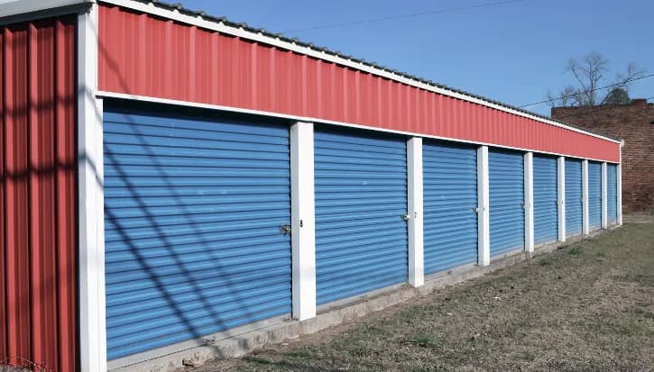 Row of blue roller door storage units along the outside of a storage building