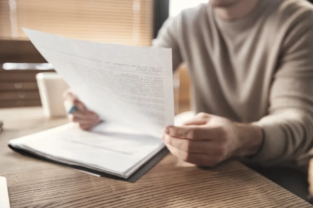 Person reading through printed documents at a timber desk